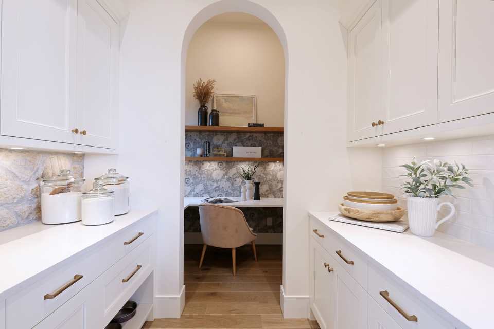 hidden home office nook with wallpaper and shelving through butler's pantry of designer white kitchen